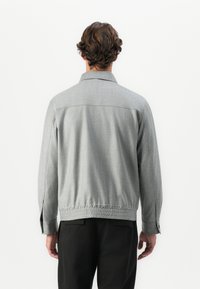 Gray button-up jacket with a textured fabric, elastic waistband, and long sleeves. Features a collar and side slits for mobility.