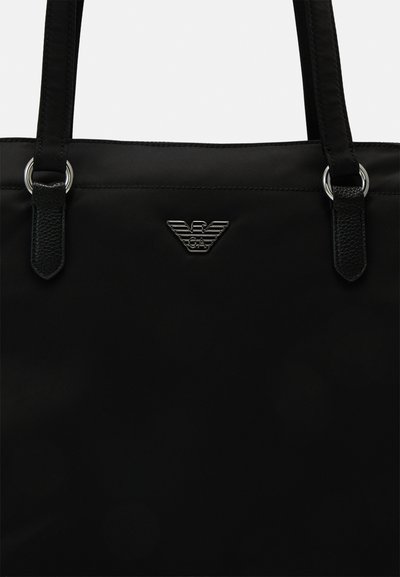 Borsa a spalla in nylon nero con due manici, dettagli in metallo argentato e un grande emblema nero sulla parte anteriore.