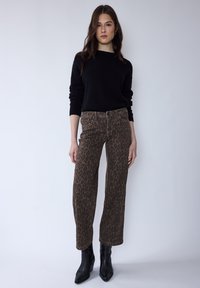 Černý pletený svetr spojený s hnědými širokými džíny s leopardím vzorem a černými špičatými kotníkovými botami, zdůrazňující texturovanou tkaninu a výrazné vzory.