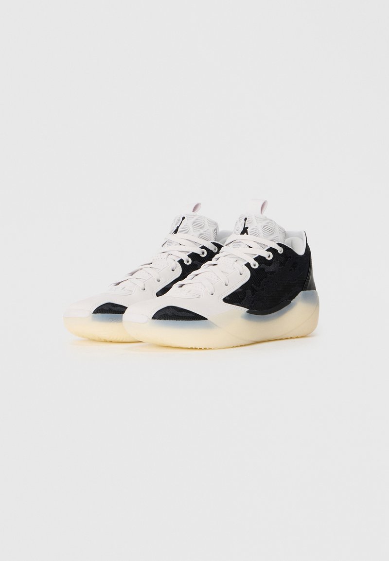 Zapatillas deportivas en blanco y negro con parte superior de tejido texturizado, puntera redondeada y suela translúcida. Cordones y logo en colores contrastantes.