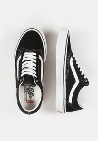 Zapatillas de skate de ante negro con acentos blancos, con cordones planos, suela de goma blanca y una etiqueta interna de marca. Diseño clásico.