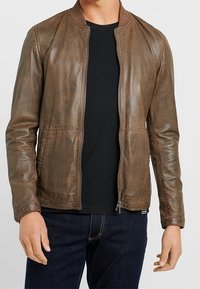 Giubbotto in pelle marrone con finitura leggermente lucida, colletto a coste, chiusura frontale con zip, due tasche laterali e una vestibilità affusolata.