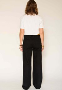Pantalon noir à jambes larges avec une taille haute, des poches arrière et une texture lisse, associé à une chemise blanche unie à manches courtes.