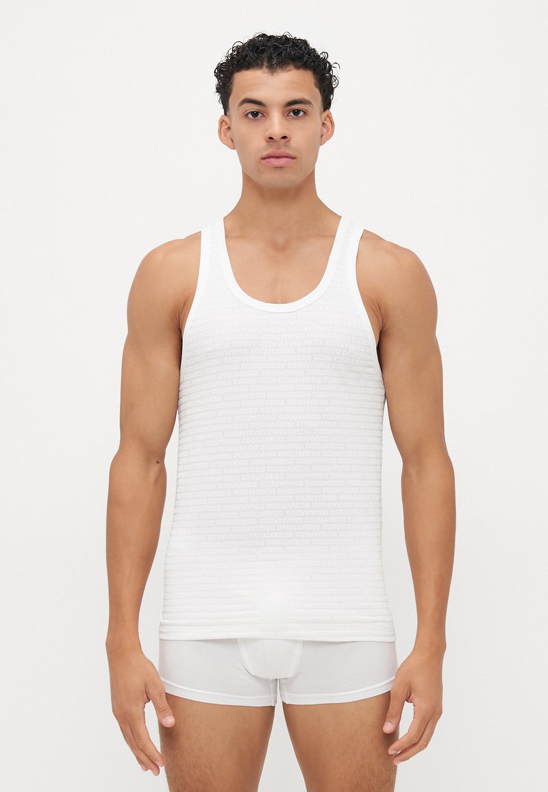 Débardeur blanc avec un motif de marque répétitif, doté d'un col rond et de larges emmanchures, associé à des sous-vêtements moulants blancs.