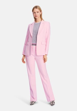 Helles rosa Anzugensemble mit einem taillierten Blazer mit Revers und zwei Fronttaschen, kombiniert mit passender Hose und gemusterten Schuhen.