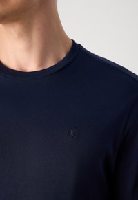 Navy blue crew-neck t-shirt made of soft fabric, featuring a subtle embroidered logo on the chest and short sleeves.