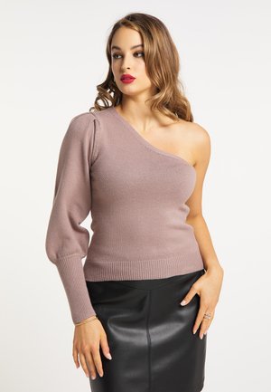 Frau mit langen welligen Haaren, die einen mauvefarbenen One-Shoulder-Pullover mit Puffärmeln und einen schwarzen Lederminirock trägt, schaut zur Seite.