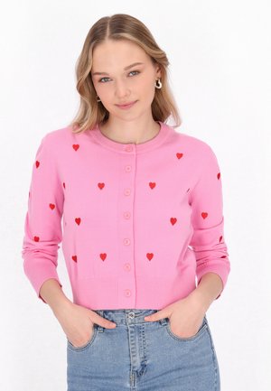 Roze cardigan met rode hartpatronen, ronde hals en knoopsluiting. Zachte brei stof met geribde manchetten en zoom.