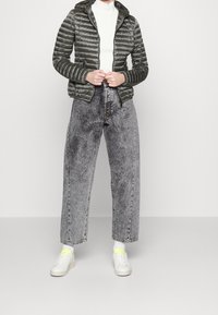 Tmavě zelená péřová bunda s vertikálním prošíváním, v kombinaci s šedými širokými džíny. Na nohou bílé tenisky s neonově žlutými akcenty.