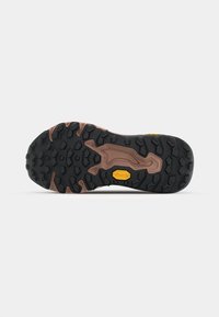 Guma potplat s dubokim utorima za prianjanje, crna s zemljanim smešnim akcentima, i Vibram logo u žutoj boji.