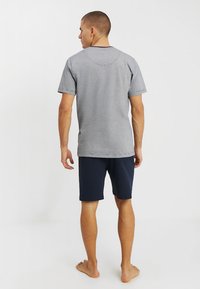 Maglietta di cotone grigia con maniche corte, scollo rotondo e dettagli di cucitura visibili, abbinata a pantaloni corti blu navy, vista da dietro.