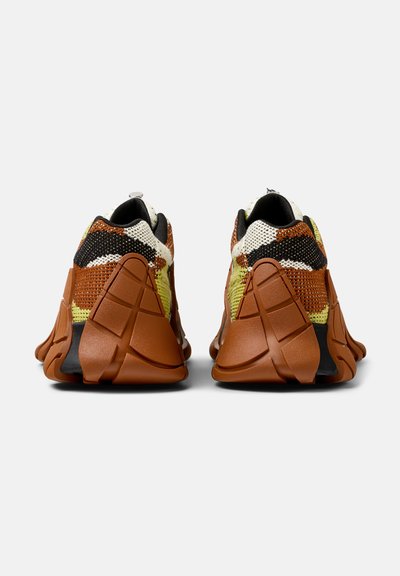 Scarpe sportive con tomaia in tessuto lavorato a maglia di colore marrone, nero e giallo, con dettagli in gomma sul tallone e suola testurizzata per una migliore aderenza.