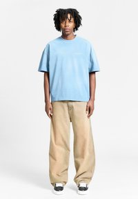 Light blue cotton oversized t-shirt with short sleeves, paired with beige wide-leg pants and black and white sneakers.