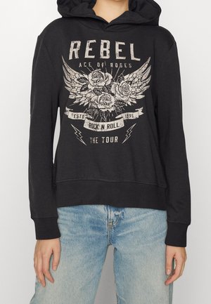 Czarna bluza z kapturem z grafiką skrzydeł i róż oraz tekstem rebel, ace of roses, rock n roll, the tour, noszona z jasnoniebieskimi dżinsami.