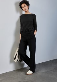 Schwarzes, geripptes Langarmoberteil, hoch taillierte schwarze weite Hose, helle Sneaker und eine gestreifte Tote-Tasche mit glatter Textur.