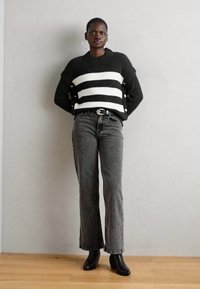 Svart-hvite stripete strikkegenser med sideskinn, kombinert med høyt liv grå svalejeans og svarte ankelstøvler.