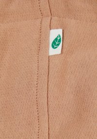 Kerge pruuni tekstuuriga kangas, millel on nähtav õmblus. Sisaldab valget sildi, millel on roheline lehekaunistus, mis näitab ökoloogiliselt sõbralikku toodet.