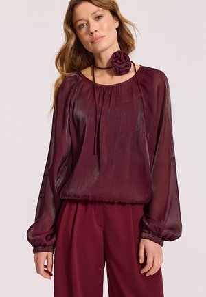 Burgundowa przezroczysta bluzka z zebranym dekoltem, długimi rękawami i elastycznymi mankietami. Zawiera dopasowany kwiatowy akcent z tego samego materiału na dekolcie.