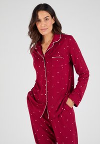 Ensemble de pyjama rouge en tissu doux avec des motifs d'étoiles blanches, comprenant une chemise à boutons, une poche et un piping blanc contrastant le long du col.