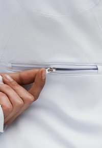 White athletic top featuring a zippered pocket. The zipper has a silver pull tab, with visible stitching along the seams. Smooth texture.