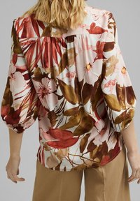 Blusa floreale con motivi in acquerello rossi, marroni e rosa. Presenta maniche a sbuffo e un design con schiena arricciata, realizzata in tessuto leggero.