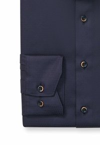 Donkerblauwe button-up shirt met een textuurpatroon, puntige kraag en verstelbare manchetten met donkere knopen en contrasterende knoopaccenten.