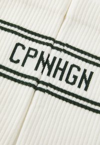 Žebrované biele ponožky s tmavozelenými pruhmi a vyšívaným textom "CPNNHGN" v tučných písmenách uprostred.