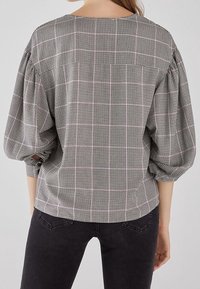 Blusa a scacchi bianca e nera con vestibilità ampia, scollatura rotonda e maniche a sbuffo. Il tessuto ha un aspetto strutturato.