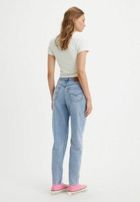 Lichtblauwe jeans met een klassieke snit, denimstof, achterzakken en een bruine leren patch op de taille. Gecombineerd met een aansluitend wit t-shirt.