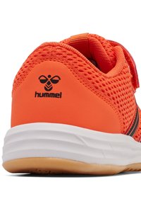 Zapatilla deportiva naranja con detalles de malla, que presenta una marca negra, suela texturizada y un collar acolchado para mayor comodidad. Cierre con tira de velcro.