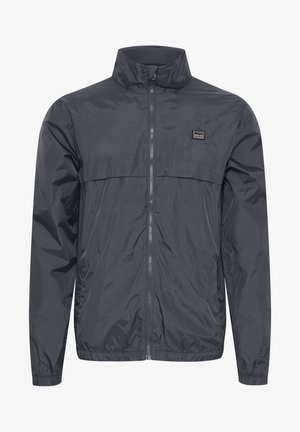 Veste légère pour hommes en gris foncé. Fabriquée en tissu résistant à l'eau, avec un col haut, une fermeture éclair intégrale et des poignets élastiques.