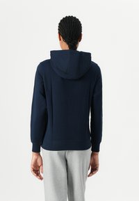 Haut à capuche bleu marine avec cordon de serrage, manches longues et poignets côtelés ; associé à un pantalon de survêtement gris clair. Design simple et non décoré.