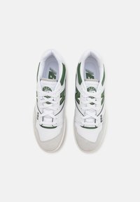 Valkoiset tennarit, joissa on vihreitä yksityiskohtia, nahka- ja verkkomateriaalit, pyöreä nilkka, teksturoitu harmaa mokkasiinipohja ja nauhajärjestelmä pehmeän kielen päällä.