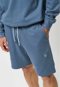 Blauwe katoenen shorts met een elastische tailleband, koord en zijzakken. Beschikt over een klein groen logo op de linker bovenbeen.