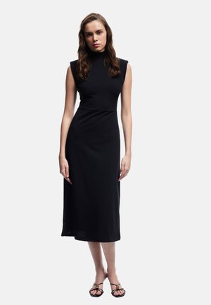 Vestido negro sin mangas con cuello alto, cuerpo ajustado y dobladillo a la altura de la rodilla. Fabricado con una tela suave y ligera. Diseño sencillo.