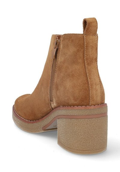 Botín de ante marrón hasta el tobillo con punta redonda, cierre de cremallera en el lateral y un tacón grueso y texturizado. Presenta un acento de color contrastante en la suela.