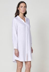 Rochie albă din bumbac cu mâneci lungi, cu nasturi la front, guler și un material texturat din in. Prezintă o fanta și mansete rulată.