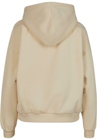 Sweat à capuche beige avec cordon de serrage, poignets et ceinture côtelés. Texture de tissu lisse, design à enfiler et coupe décontractée.