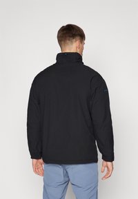 Doudoune noire avec un col montant et des manches longues. Présente une texture lisse et un logo d'accent bleu sur l'épaule.