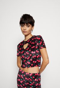 Top cropped preto com mangas curtas, apresentando um recorte em forma de coração e um padrão de cerejas em vermelho e verde. Feito com um material brilhante.
