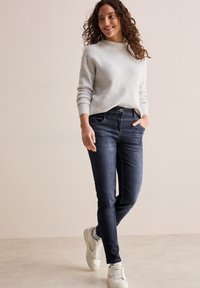 Lichtgrijze, gestructureerde trui met een ronde hals, gecombineerd met donkerblauwe jeans en witte sneakers, met zakken en een knoopsluiting.