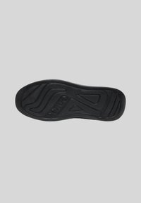 Semelle de chaussure en caoutchouc noir avec des motifs texturés, y compris des lignes et des formes ondulées, et le logo "Gues's" embossé près du talon.