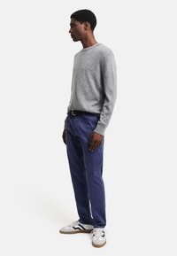 Grauer Strickpullover, marineblaue Hose mit Taschen, weiße und graue Sneakers mit grünen Akzenten. Fokussiert auf Komfort und lässigen Stil.