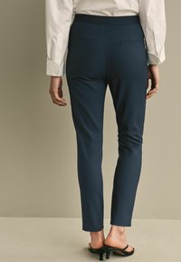 Námořnické zúžené kalhoty s hladkým textilním povrchem, obsahující dvě zadní kapsy a slim fit střih. V kombinaci s černými sandály na podpatku.