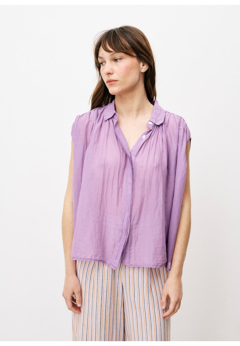 Helllila ärmellose Bluse mit Knopfleiste und gerafftem Schulterdetail, kombiniert mit gestreiften Hosen. Glatte Stoffoberfläche.