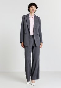 Completo grigio a righe con giacca su misura e pantaloni a gamba larga, abbinato a una camicia colletto rosa chiaro e scarpe con tacco bianco.