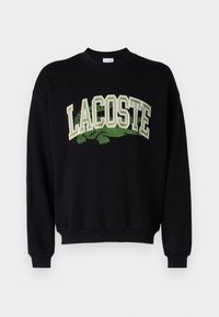 Felpa nera con logo "LACOSTE" verde testurizzato in carattere distintivo, maniche lunghe e colletto e orlo a costine.