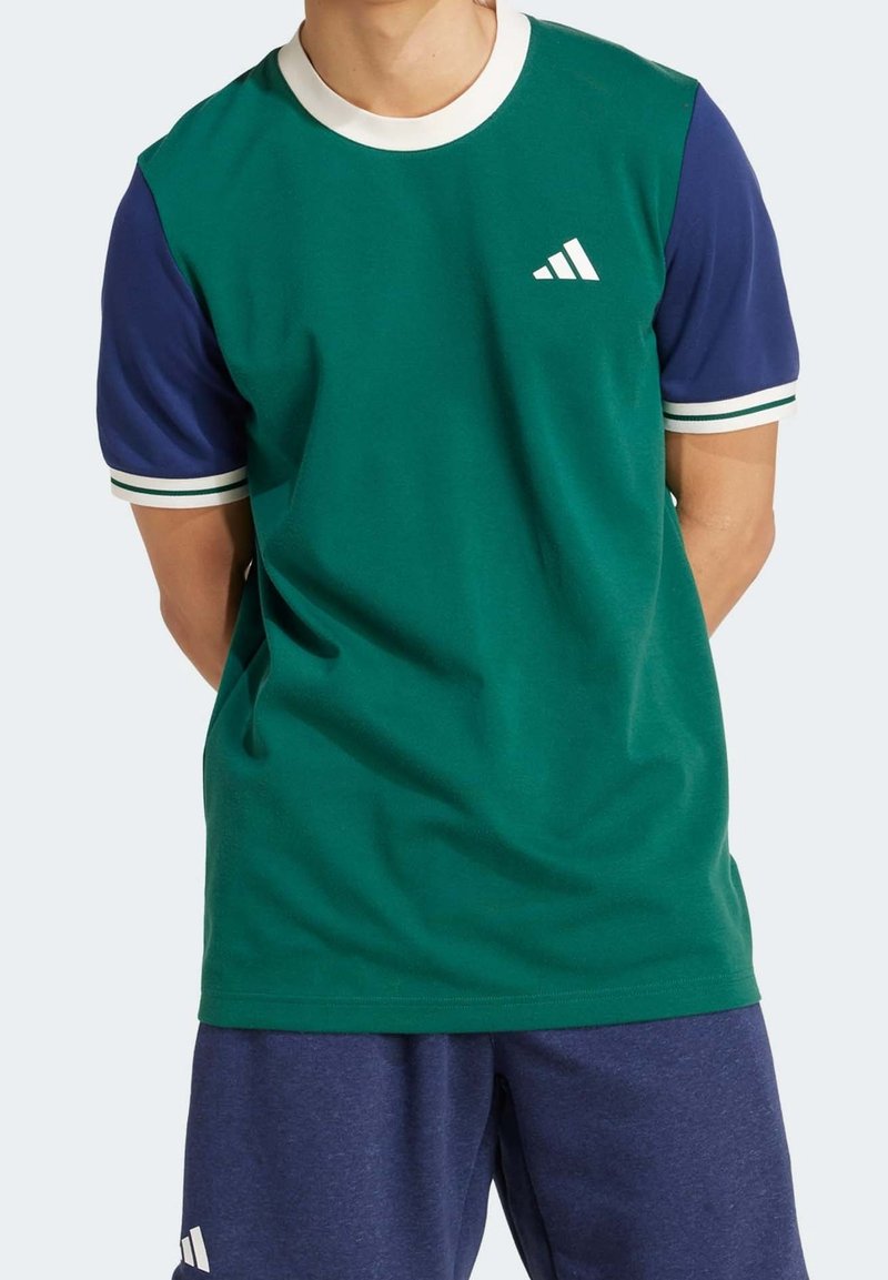 Chemise à manches courtes vert et marine avec col blanc et accents rayés. Présente un logo blanc sur la poitrine. Texture de tissu lisse.