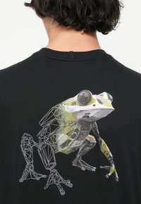 Μαύρο μπλουζάκι με λευκή και κίτρινη γεωμετρική γραφική απεικόνιση βατράχου. Ο σχεδιασμός περιλαμβάνει πολύπλοκες λεπτομέρειες και υφή.