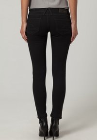Jeans skinny negros de cintura alta, con una textura suave, dos bolsillos traseros y detalles de costura sutiles. Combinados con zapatos de tacón alto.
